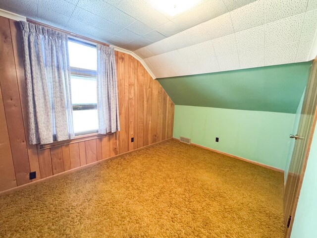 additional living space featuring vaulted ceiling, baseboards, wooden walls, and carpet