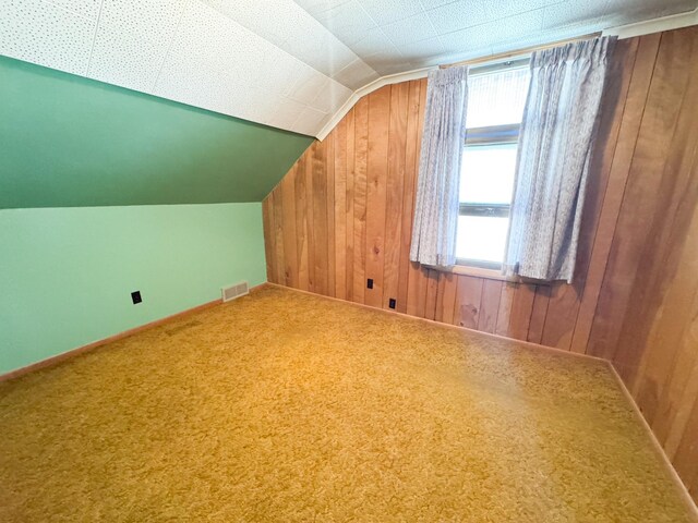 additional living space featuring wood walls, lofted ceiling, and carpet