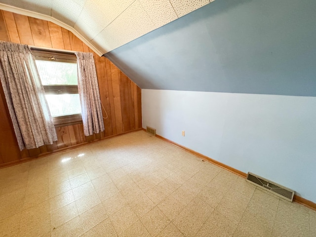 additional living space with lofted ceiling, baseboards, tile patterned floors, and wood walls