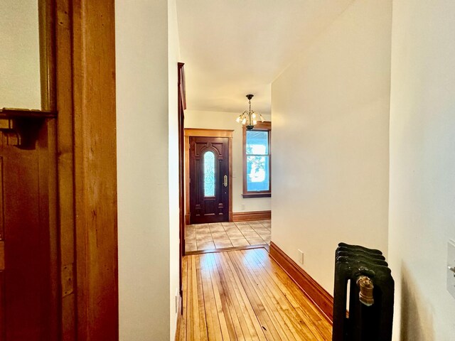 hall with an inviting chandelier, baseboards, and light wood-type flooring