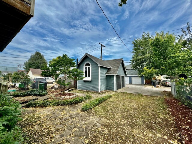 view of property exterior featuring fence, an outbuilding, a shingled roof, and a garage