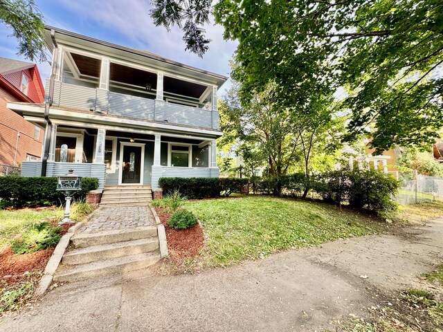 view of front of property with fence, a porch, a front lawn, and a balcony