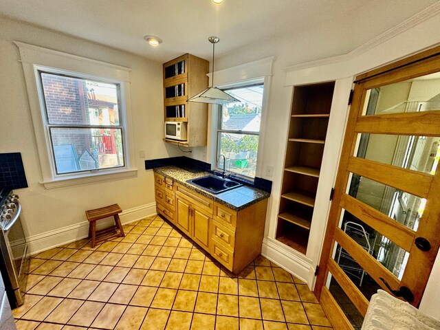 kitchen with dark countertops, brown cabinets, a sink, light tile patterned floors, and white microwave