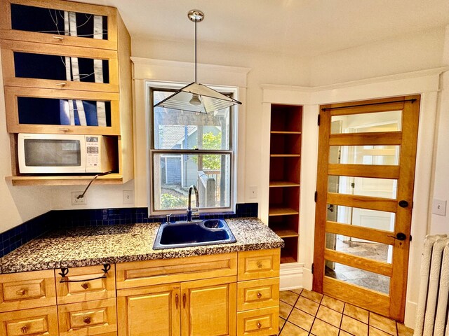 kitchen with a sink, tile counters, white microwave, and decorative light fixtures
