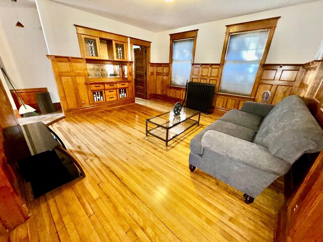 living room with light wood-type flooring, a wainscoted wall, and radiator heating unit