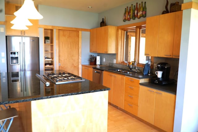 kitchen with stainless steel appliances, a sink, dark stone counters, light wood-style floors, and a center island