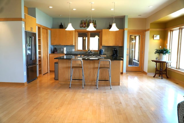 kitchen featuring black refrigerator with ice dispenser, dark countertops, decorative backsplash, a breakfast bar, and light wood-type flooring