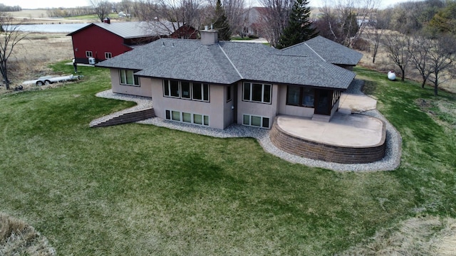 rear view of house with roof with shingles, a patio, a lawn, and stucco siding