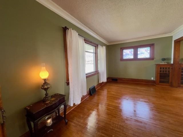 unfurnished room featuring crown molding, a textured ceiling, baseboards, and wood finished floors