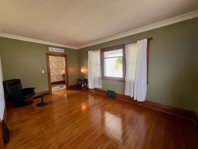 interior space with baseboards, ornamental molding, a textured ceiling, and wood finished floors