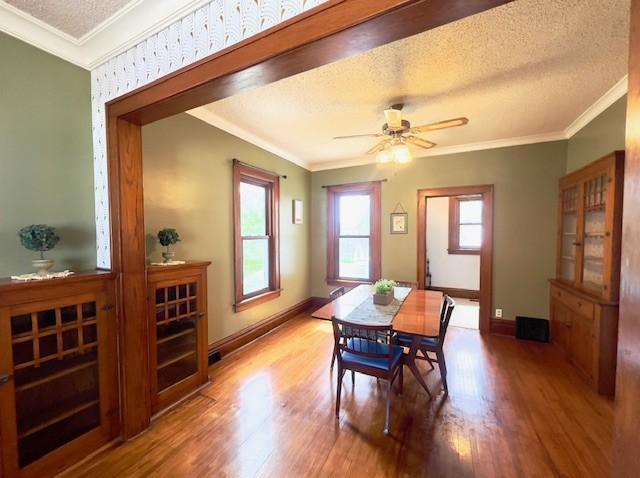 dining space with baseboards, ornamental molding, a textured ceiling, and wood finished floors