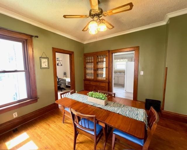dining room featuring a ceiling fan, a textured ceiling, baseboards, light wood-style floors, and ornamental molding