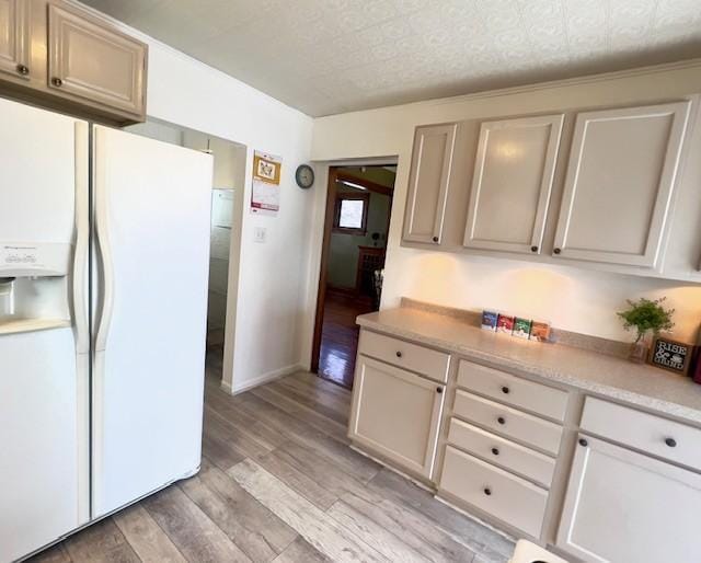 kitchen with light countertops, baseboards, white refrigerator with ice dispenser, and light wood finished floors