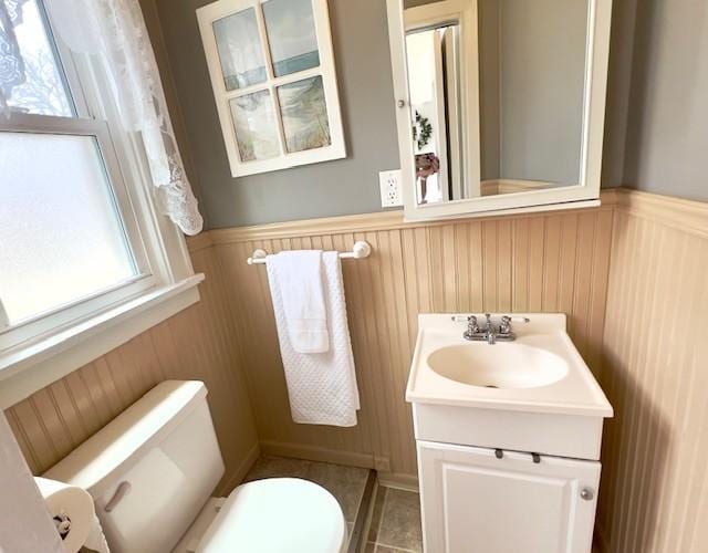 bathroom with a wainscoted wall, a healthy amount of sunlight, and toilet