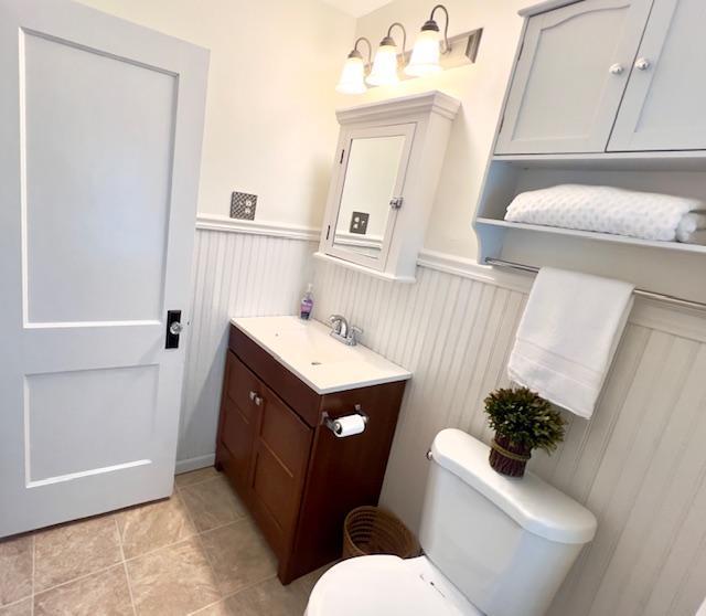 half bath with toilet, tile patterned floors, wainscoting, and vanity