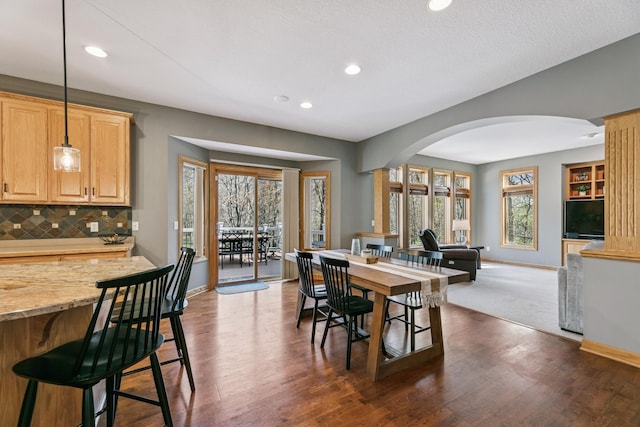dining area featuring dark wood finished floors, arched walkways, baseboards, and recessed lighting