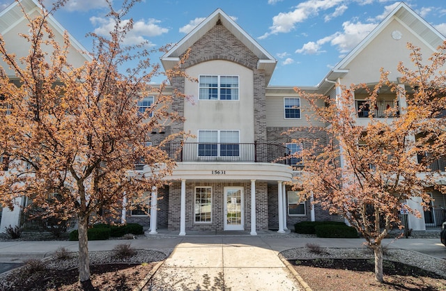 townhome / multi-family property featuring a porch, stucco siding, a balcony, and brick siding