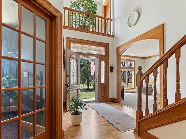 entrance foyer featuring wood finished floors, arched walkways, stairs, baseboards, and a towering ceiling