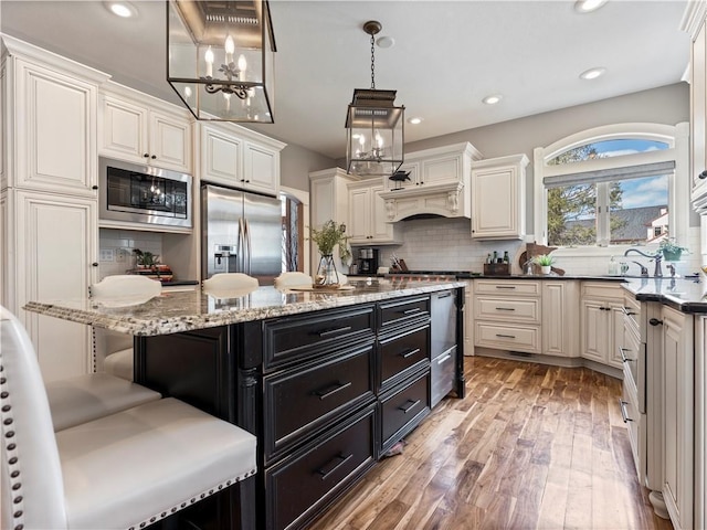 kitchen featuring tasteful backsplash, a breakfast bar, appliances with stainless steel finishes, dark cabinetry, and light wood-type flooring