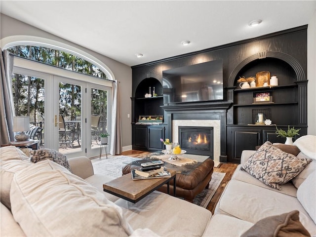 living area featuring a glass covered fireplace, wood finished floors, built in features, and baseboards