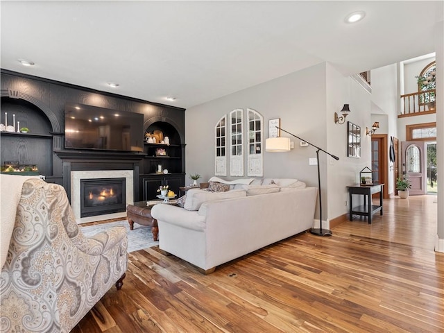 living area with recessed lighting, built in shelves, wood-type flooring, baseboards, and a fireplace with flush hearth