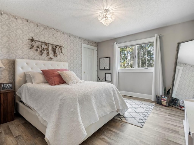 bedroom featuring a textured ceiling, wood finished floors, wallpapered walls, and baseboards