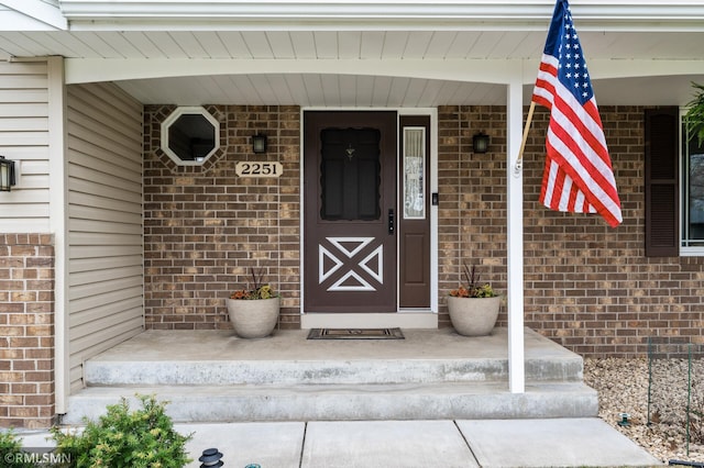 doorway to property featuring covered porch and brick siding