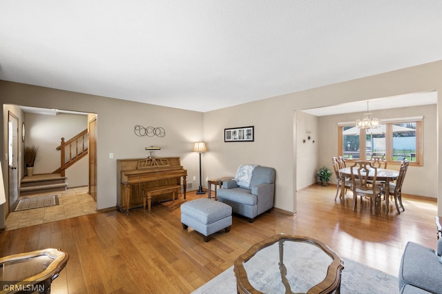 living area featuring stairs, an inviting chandelier, and light wood-style floors