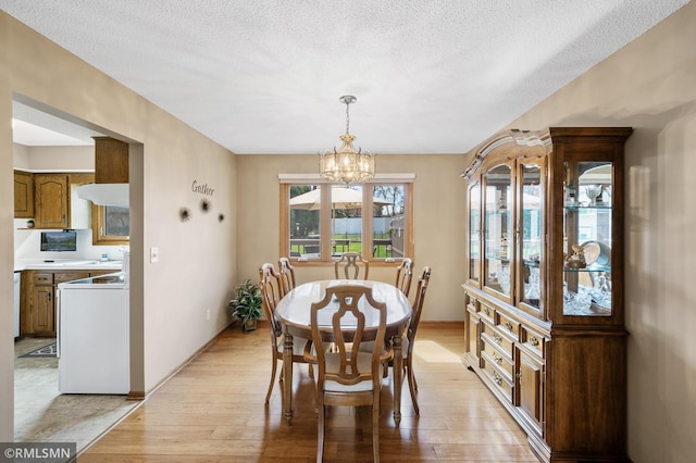 dining space with light wood finished floors, a textured ceiling, a chandelier, and baseboards