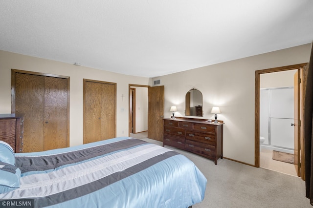 bedroom featuring light colored carpet, two closets, ensuite bathroom, baseboards, and visible vents