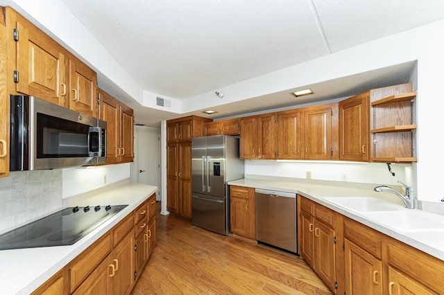 kitchen with appliances with stainless steel finishes, a sink, light wood-type flooring, open shelves, and brown cabinetry