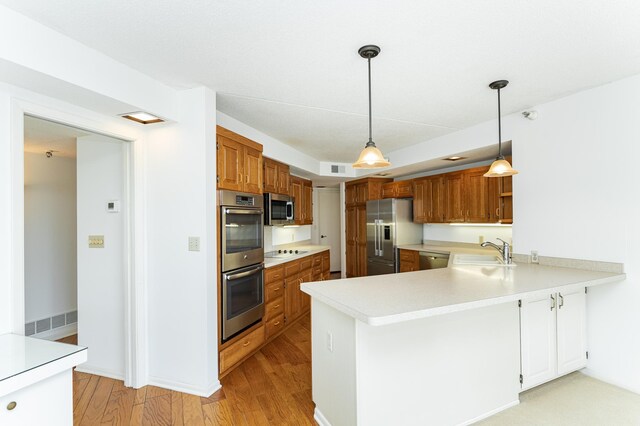 kitchen featuring appliances with stainless steel finishes, a sink, a peninsula, light countertops, and light wood-style floors
