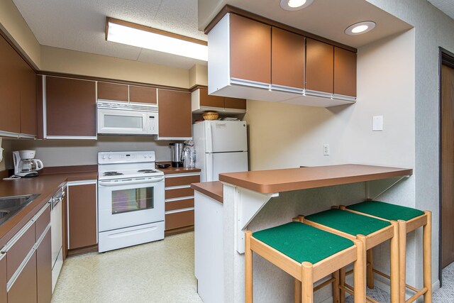 kitchen featuring white appliances, a peninsula, a breakfast bar area, dark countertops, and a sink