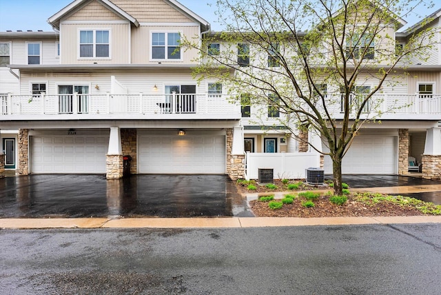 multi unit property with driveway, central air condition unit, an attached garage, and stone siding