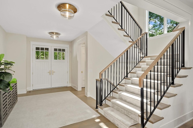 foyer featuring baseboards, stairway, wood finished floors, and a healthy amount of sunlight