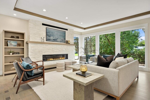 living room featuring recessed lighting, a stone fireplace, wood finished floors, and a tray ceiling