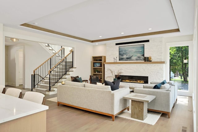 living area with light wood-style floors, a fireplace, and a tray ceiling