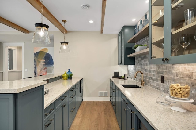 kitchen featuring light stone countertops, decorative backsplash, light wood finished floors, a sink, and a peninsula