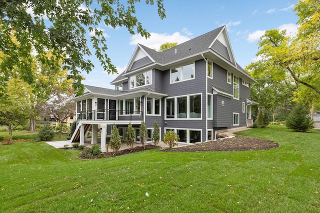 rear view of property with stairway, a shingled roof, a sunroom, and a lawn