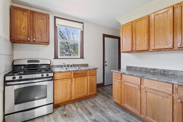 kitchen with stainless steel range with gas cooktop, dark countertops, light wood finished floors, and a sink