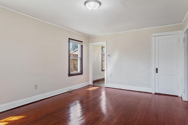 empty room with wood finished floors, crown molding, and baseboards