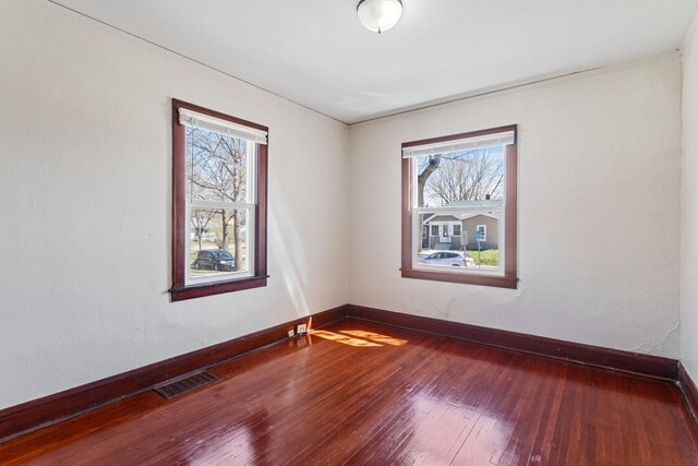 spare room with hardwood / wood-style floors, visible vents, and baseboards