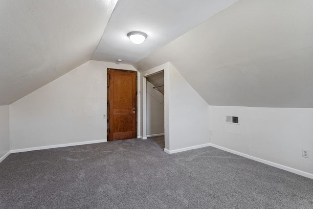 additional living space with baseboards, visible vents, dark carpet, and vaulted ceiling
