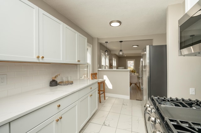 1634 Upton Ave N, Minneapolis, MN 55411 - kitchen featuring appliances with stainless steel finishes, white cabinetry, light marble finish flooring, backsplash, and decorative light fixtures