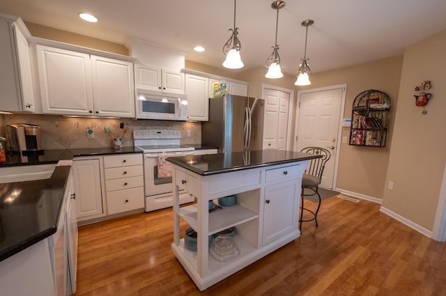 kitchen with dark countertops, tasteful backsplash, white cabinetry, and white appliances