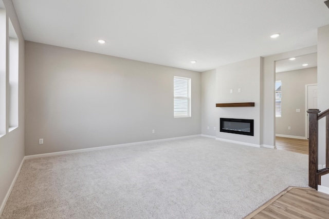 unfurnished living room with recessed lighting, light carpet, a glass covered fireplace, baseboards, and light wood-type flooring