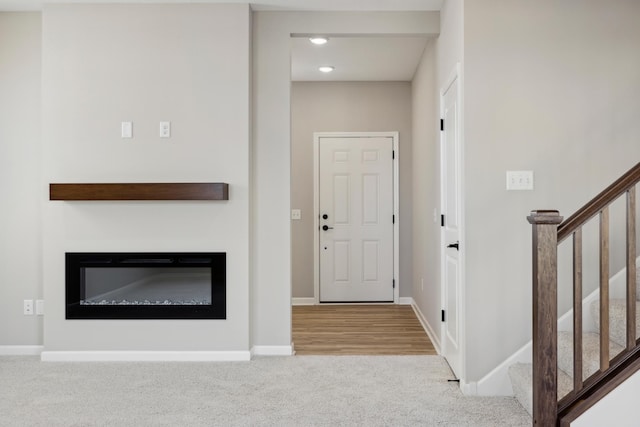 entryway featuring stairway, a glass covered fireplace, carpet, and baseboards