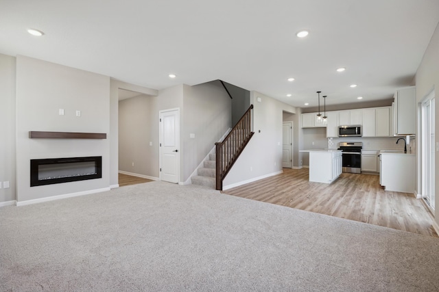 unfurnished living room featuring a glass covered fireplace, a sink, light carpet, and baseboards