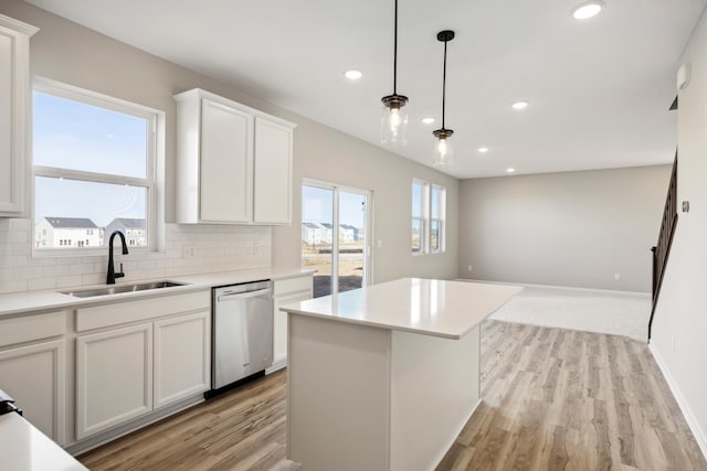 kitchen featuring tasteful backsplash, stainless steel dishwasher, white cabinets, a sink, and light wood finished floors