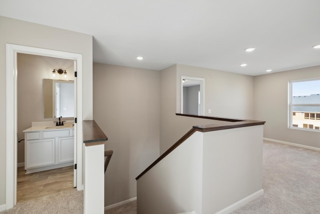 hallway featuring an upstairs landing, a sink, light carpet, and baseboards